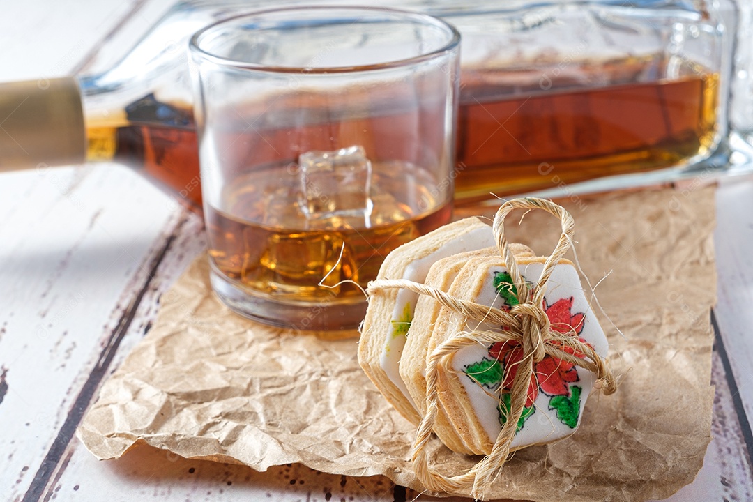 Copo de uísque com gelo em papel pardo, ao lado de uma mini torta