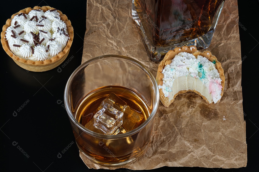 Gelo em copo de uísque, rodeado de mini tortas de ganache e uísque