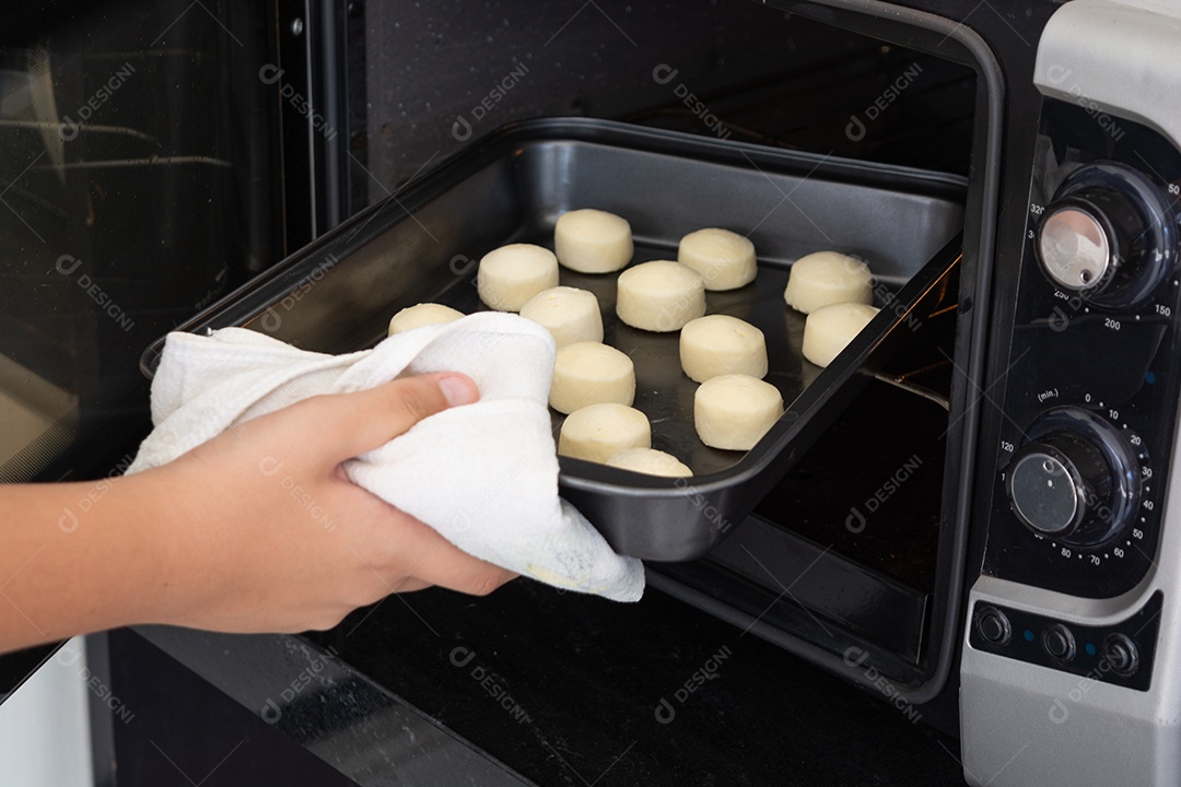 Homem tirando uma assadeira com pãezinhos de queijo de um forno elétrico