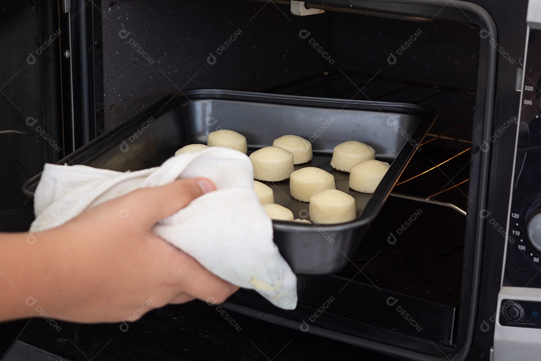 Homem tirando uma assadeira com pãezinhos de queijo de um forno elétrico