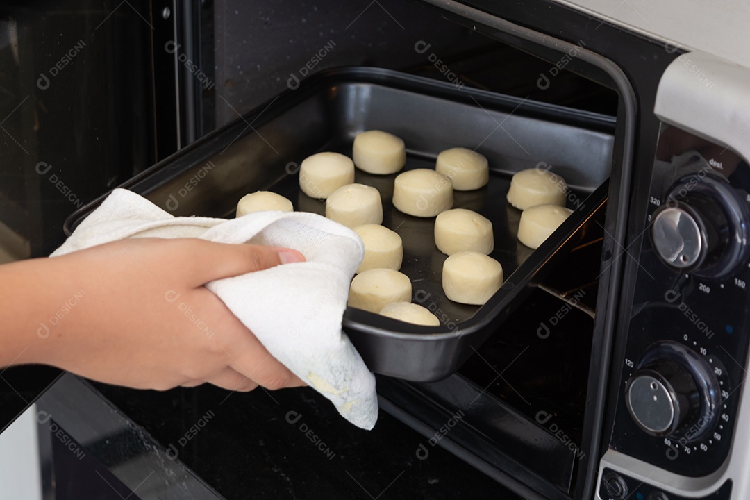 Homem tirando uma assadeira com pãezinhos de queijo de um forno elétrico