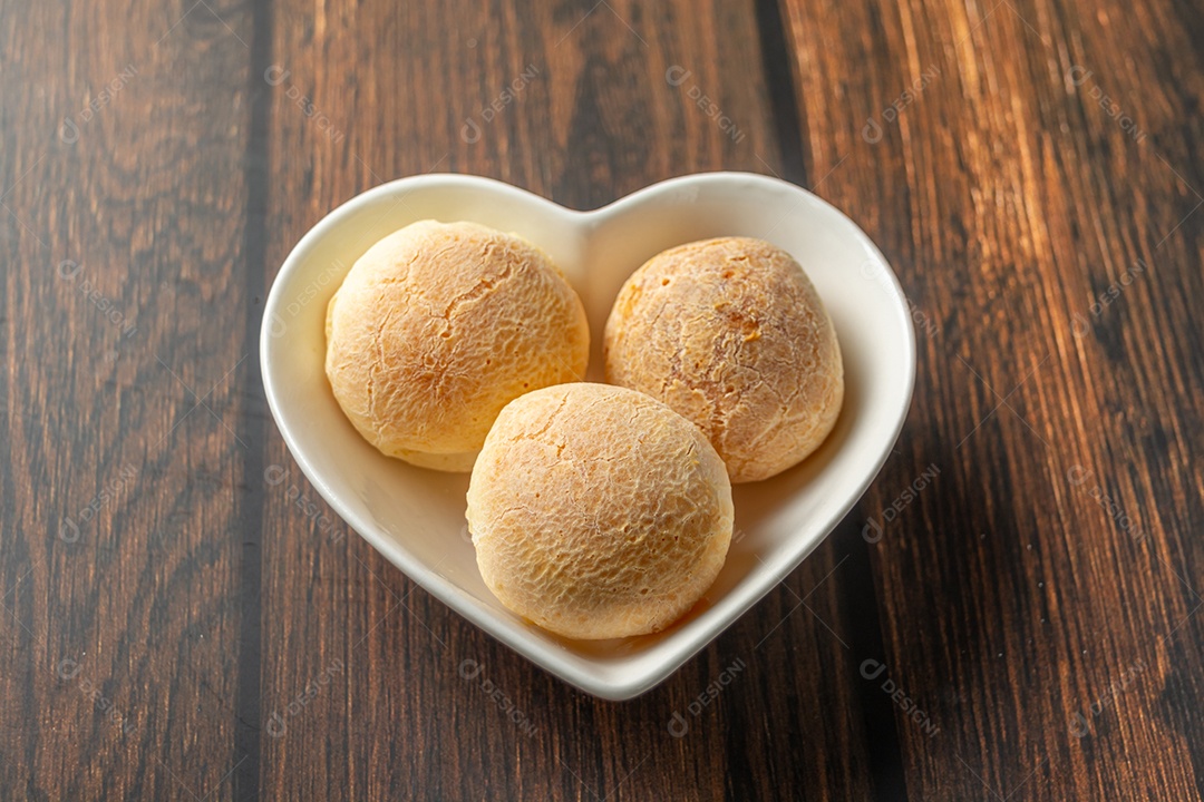 Pão de queijo em recipiente em forma de coração na mesa de madeira com copo