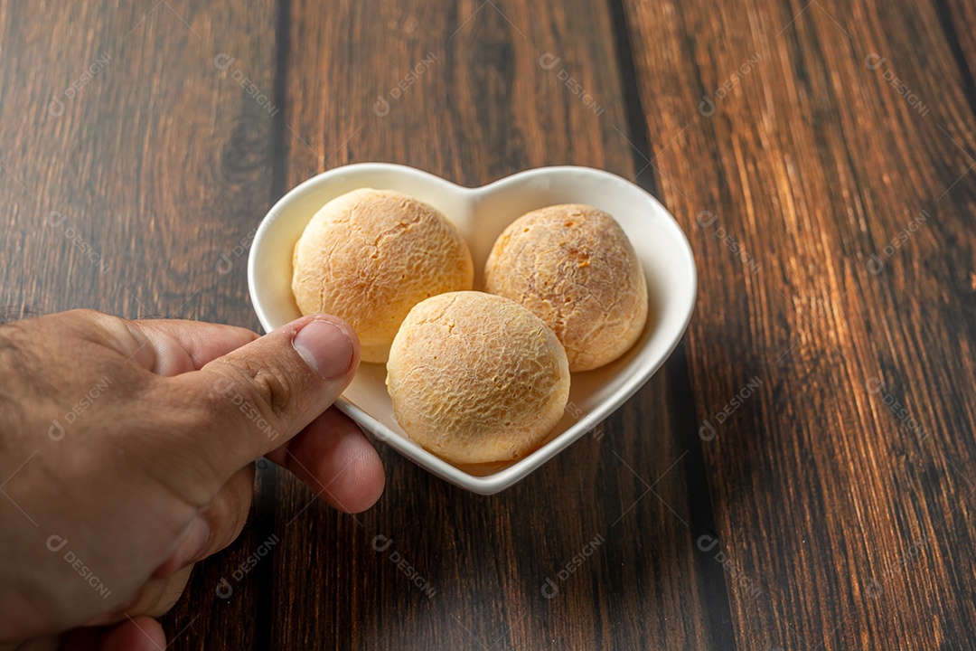 Mão masculina servindo pão de queijo em recipiente em forma de coração na madeira