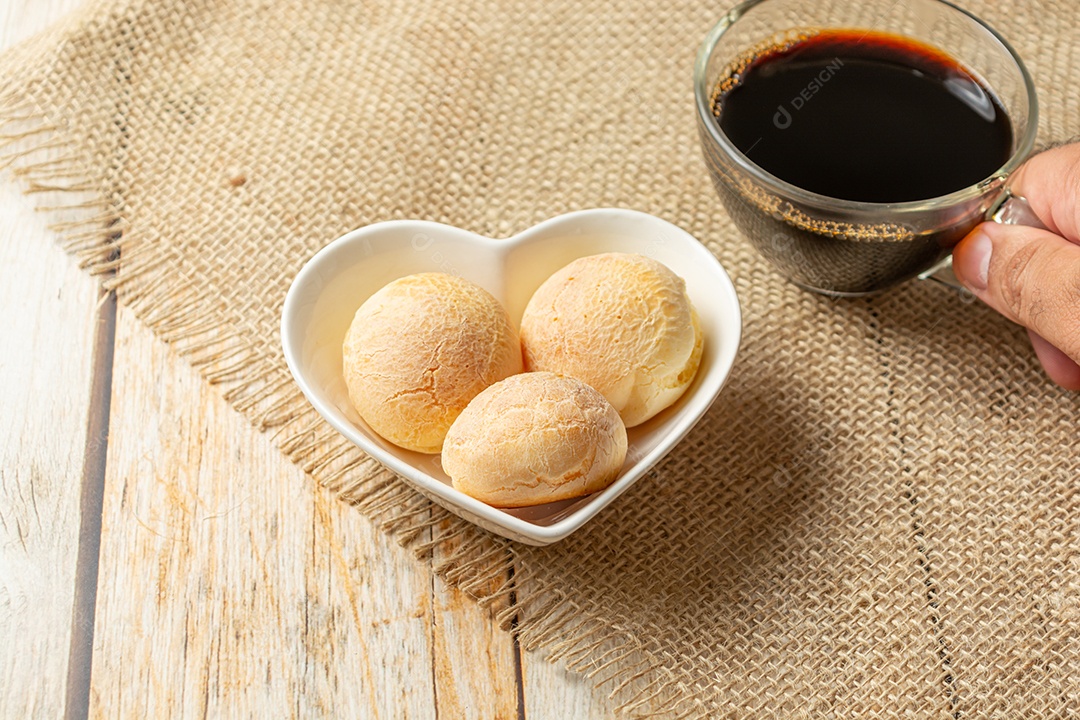 Pão de queijo em recipiente em forma de coração na mesa de madeira com copo