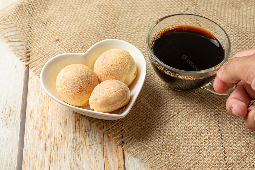Pão de queijo em recipiente em forma de coração na mesa de madeira com copo
