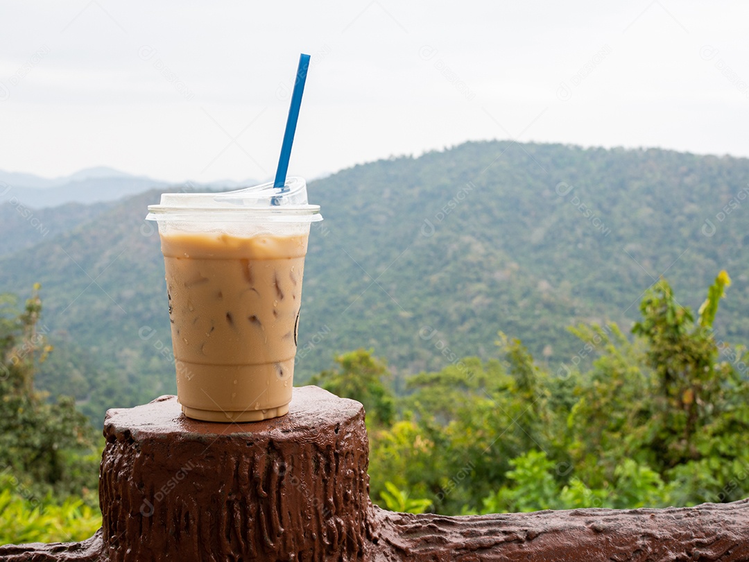 Um copo de café gelado é colocado em cima do muro em um cenário de montanhas e céu.