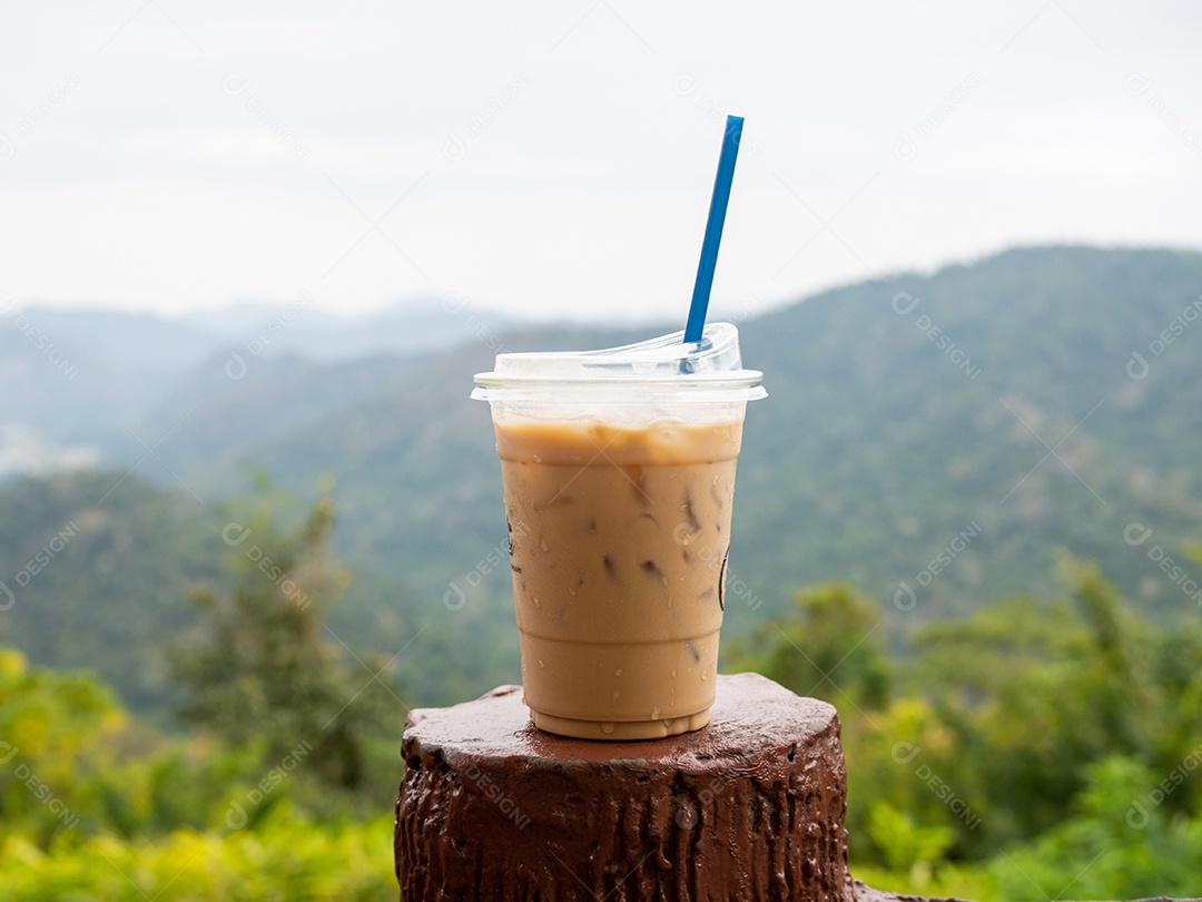 Um copo de café gelado é colocado em cima do muro em um cenário de montanhas e céu.