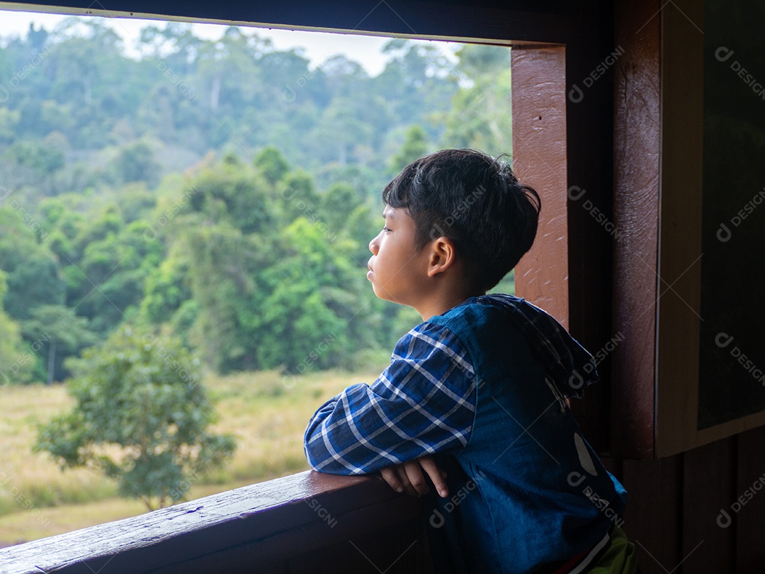 Menino olhando pela janela olhando para a floresta verde