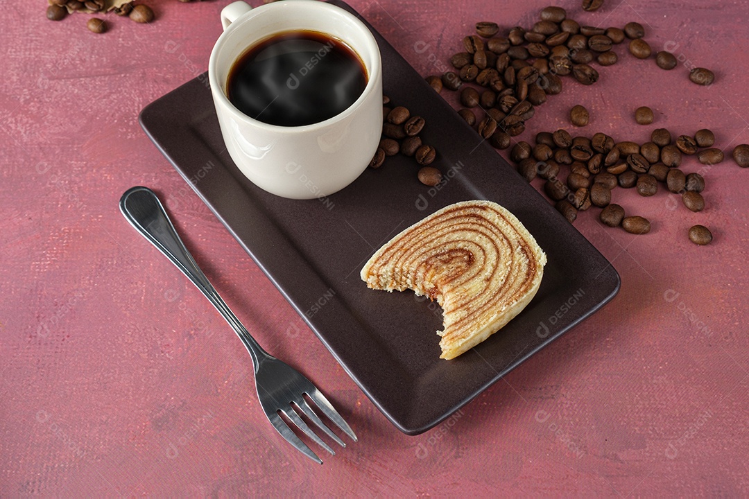 Fatia de bolo de rolo com uma mordida ao lado de um garfo, xícara e café