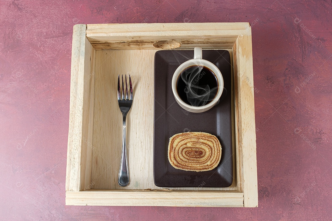 fatia de bolo de rolo em um prato marrom, ao lado de uma xícara de café e um garfo.