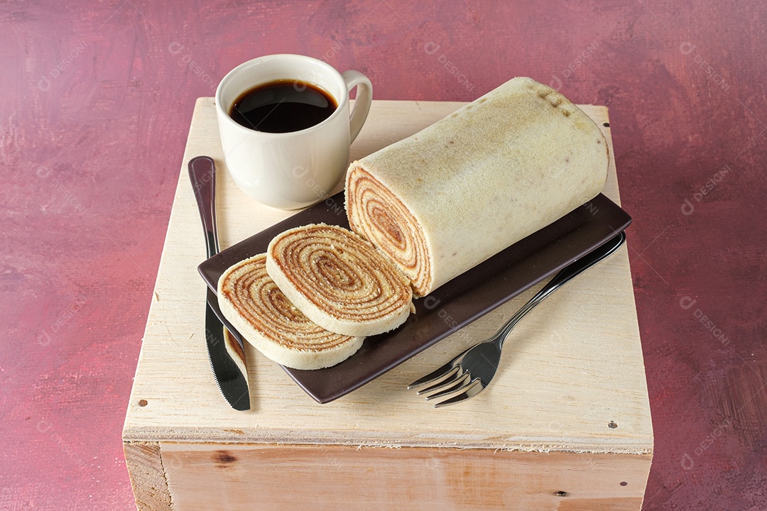 Bolo de rolo fatiado em um prato marrom, ao lado de talheres