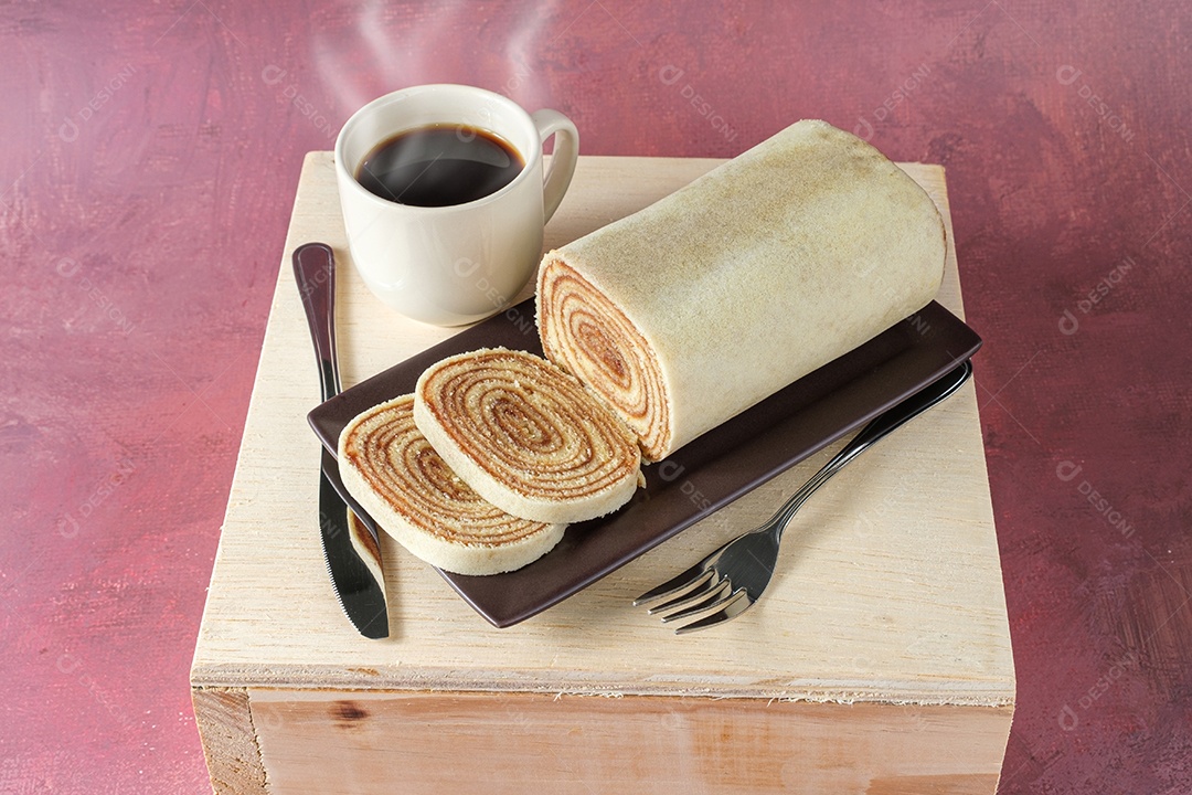 Bolo de rolo fatiado em um prato marrom, ao lado de talheres e um copo