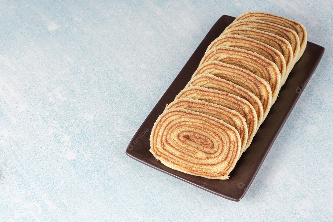 Bolo de rolo fatiado em um prato marrom e fundo azul e branco