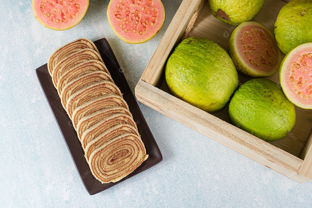 Bolo de rolo fatiado ao lado de uma caixa com goiabas
