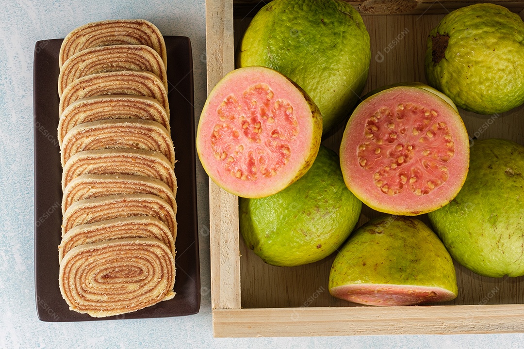 Bolo de rolo fatiado ao lado de uma caixa com goiabas