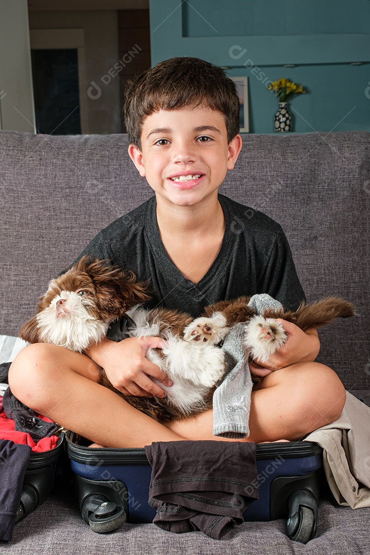 criança de 8 anos sentada em uma mala aberta com um cachorrinho shih tzu