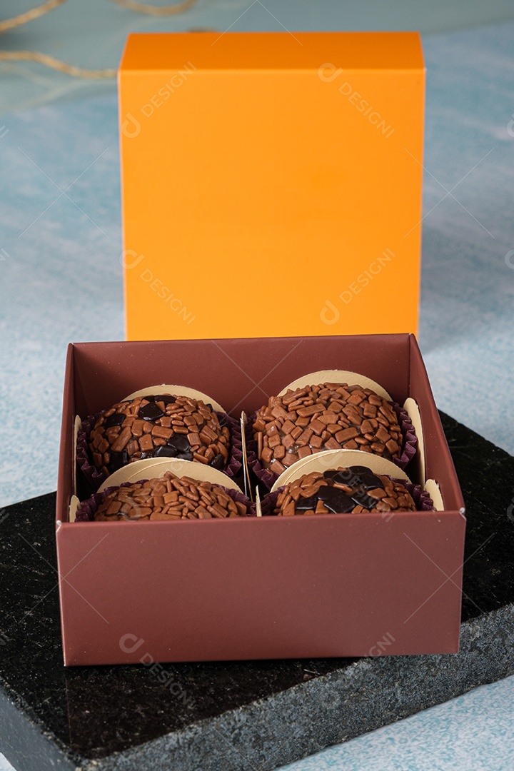 Quatro brigadeiros dentro de uma caixa sobre uma pedra de mármore.