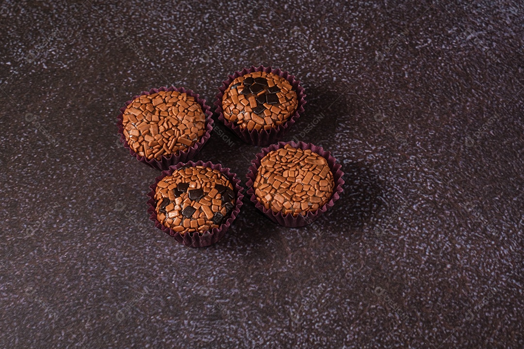 Quatro brigadeiros, tradicionais e amargos, sobre fundo preto e azul.