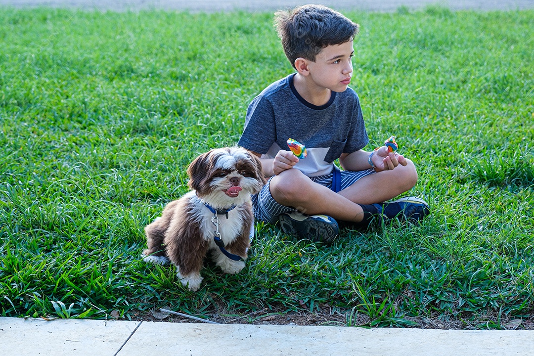 Menino de 8 anos sentado no gramado ao lado de seu animal de estimação