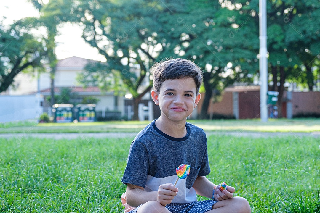 Menino de 8 anos sentado no gramado em uma tarde ensolarada, sorrindo
