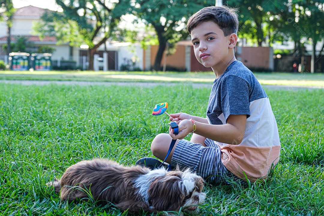 Menino de 8 anos sentado no gramado ao lado de seu animal de estimação