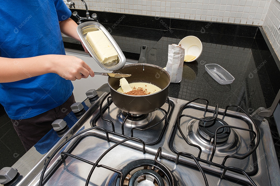 Closeup das mãos da criança colocando um pedaço de manteiga na panela