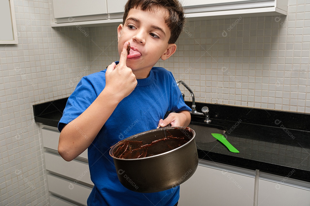 Criança de 8 anos na cozinha segurando uma panela e lambendo o dedo