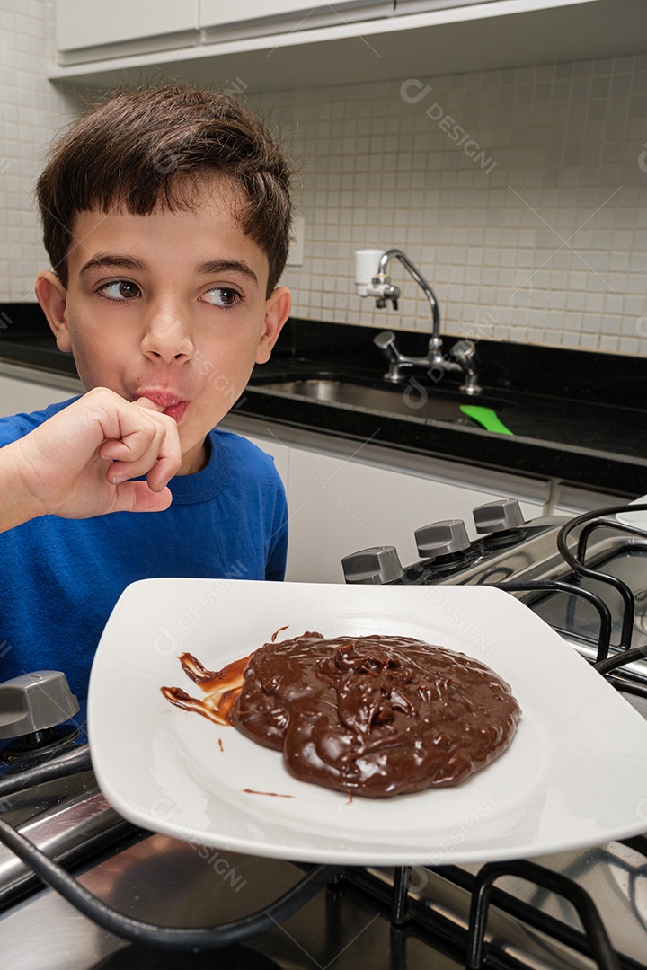 Criança de 8 anos Lambendo o dedo na frente de um prato de brigadeiro