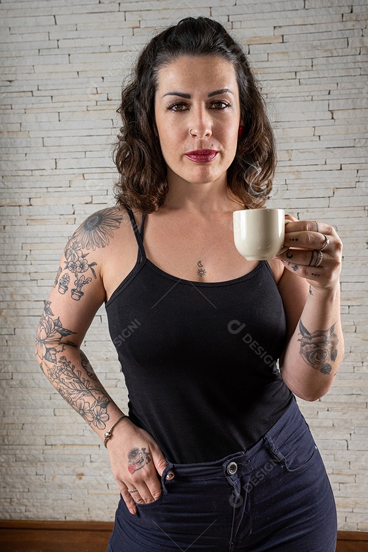 Brasileira tatuada e sensual, com a mão no bolso e segurando uma xícara de café