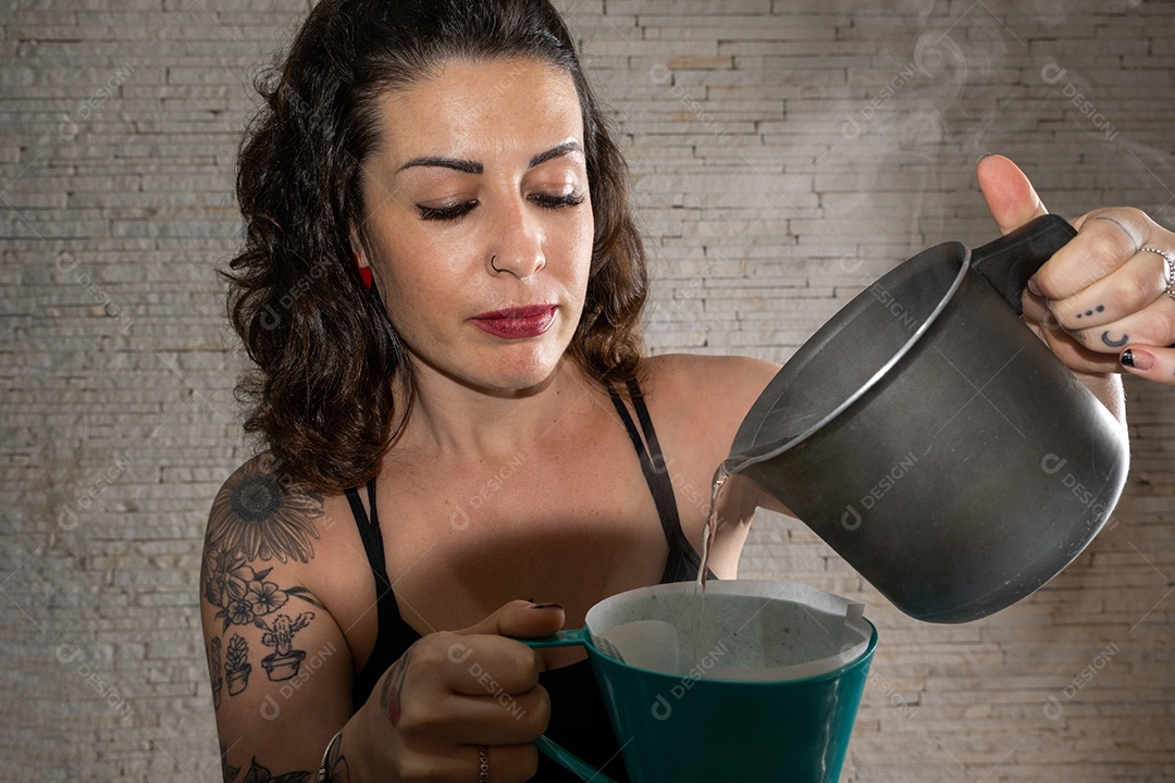 Brasileira tatuada colocando água quente no pó de café