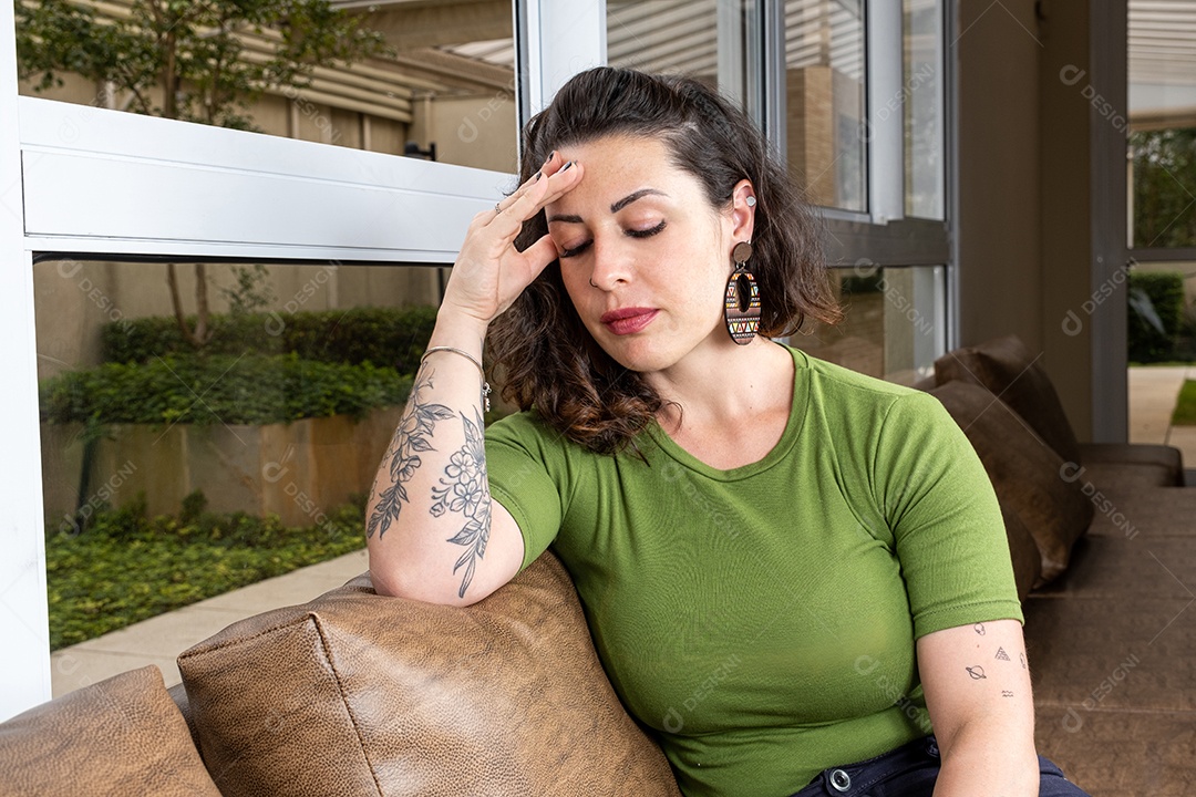 Brasileira com enxaqueca e tatuado sentado no sofá marrom