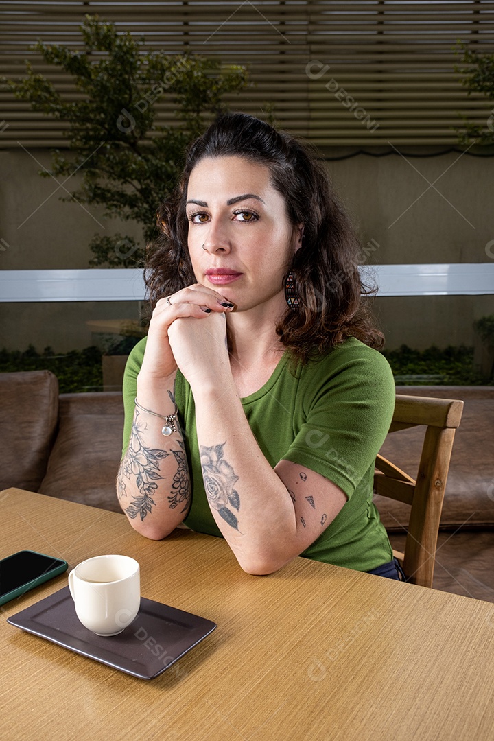 Brasileira tatuada e pensativa, com as mãos no queixo