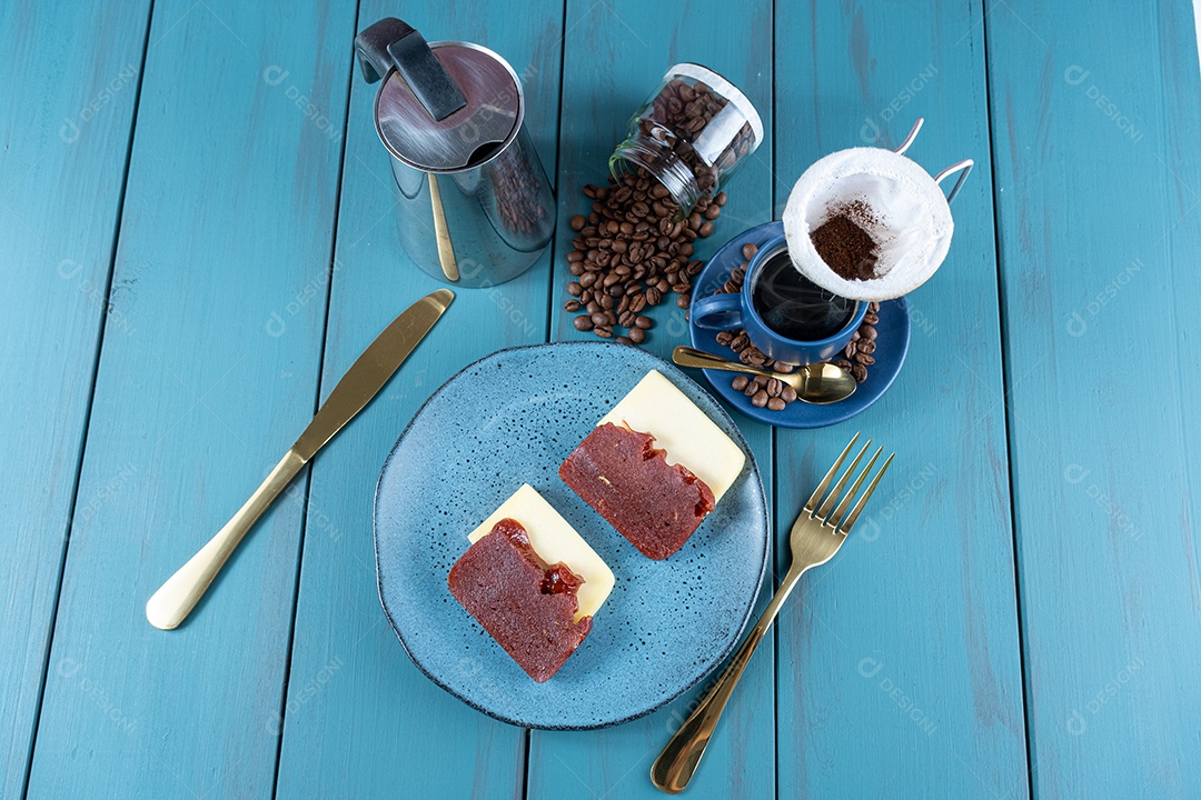 Doce de goiaba com queijo rodeado de talheres, xícara e café