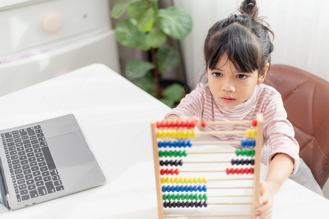 Uma jovem e bonita garota asiática está usando o ábaco com miçangas coloridas para aprender a contar em casa