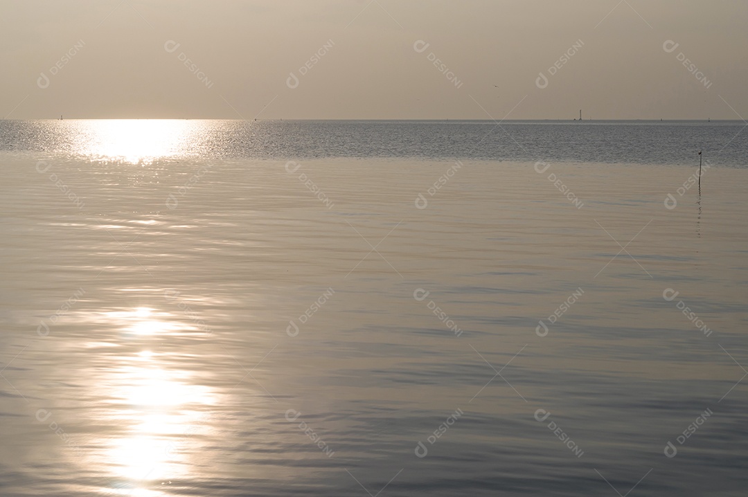 O sol maravilhoso está se pondo na superfície da água do mar à noite no litoral