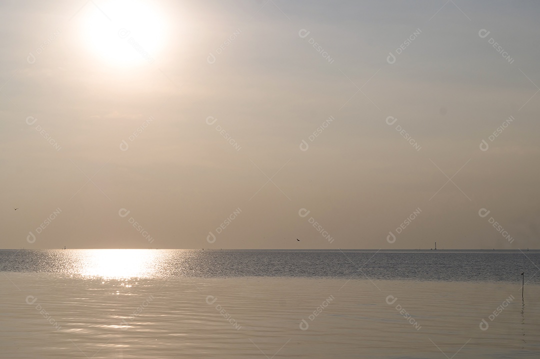 O sol maravilhoso está se pondo na superfície da água do mar à noite no litoral
