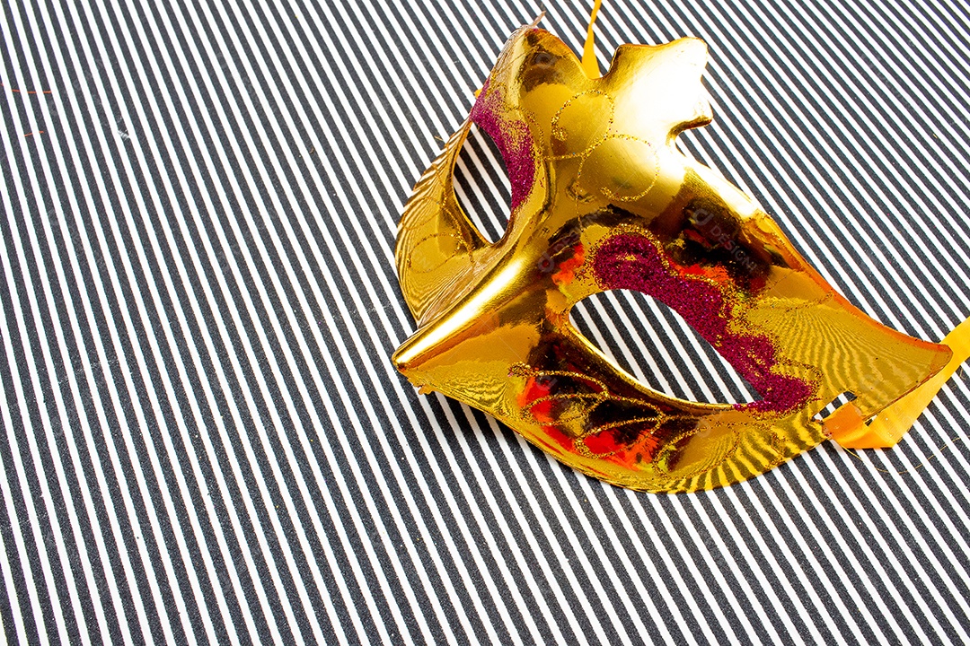 máscara de carnaval dourada em um fundo listrado preto e branco