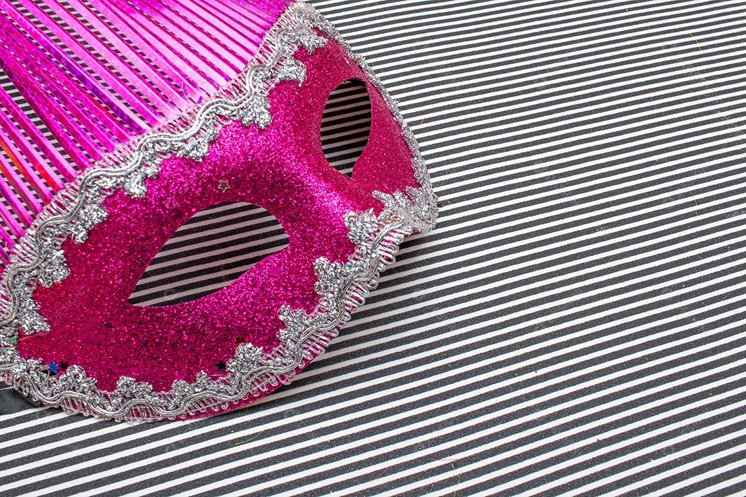 máscara de carnaval rosa em um fundo listrado preto e branco