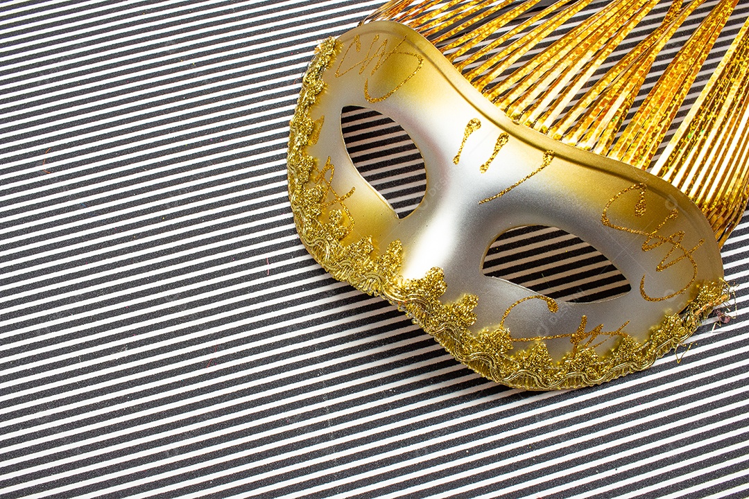 máscara de carnaval dourada em um fundo listrado preto e branco