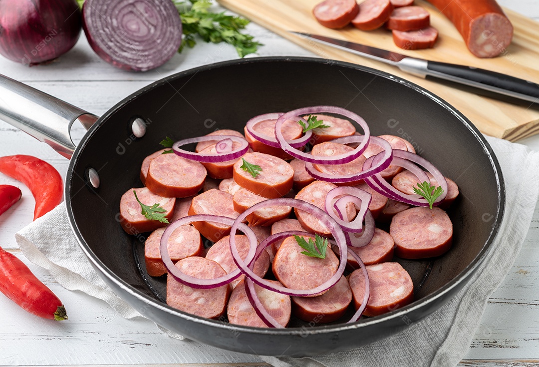 Fatias de linguiça calabresa crua em uma panela com cebola, pimenta