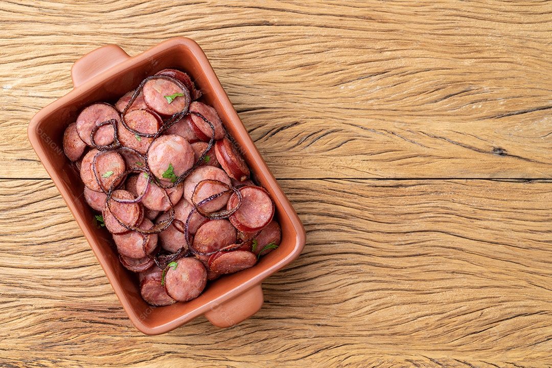 Porção de linguiça calabresa grelhada com cebola sobre mesa de madeira