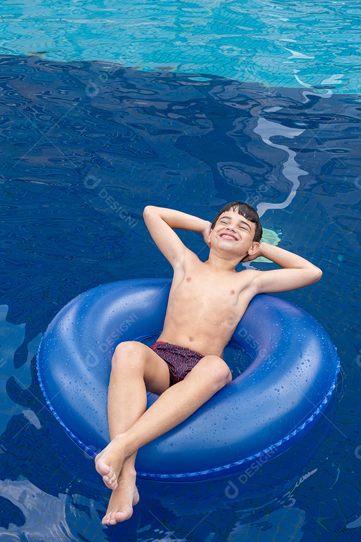 Brasileiro de 9 anos na piscina, fazendo careta, em uma boia em um dia ensolarado.