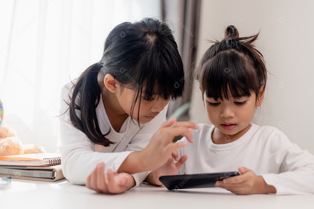 Crianças de conceito e gadgets. Duas irmãs irmãs olham para o telefone e sorriem. Eles seguram um smartphone, assistem a vídeos, aprendem, jogam, falam online. Internet para crianças. Controle dos pais