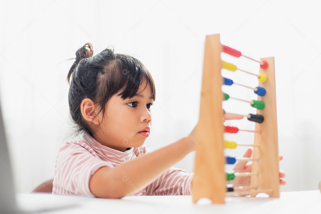 Uma jovem e bonita garota asiática está usando o ábaco com miçangas coloridas para aprender a contar em casa