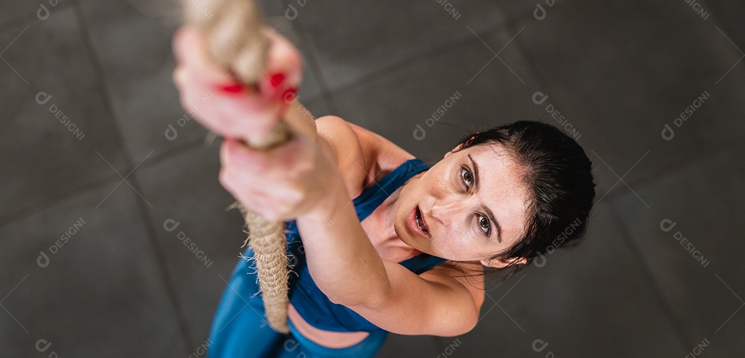 Mulher latina treinando com corda de batalha no ginásio cross fit