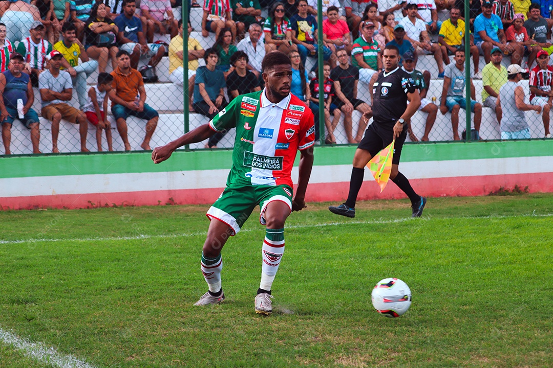 Belo homem jogando futebol sobre um gramado com torcida sobre fundo