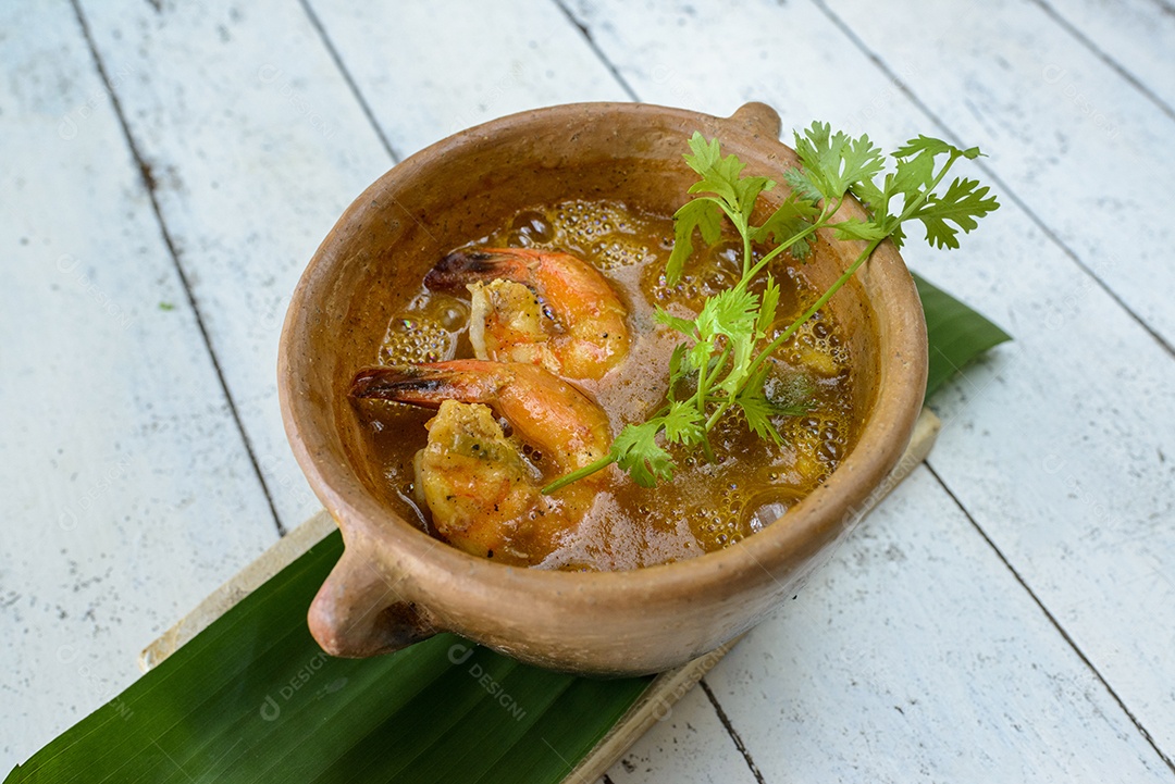 Caldo de camarão em tigela de barro na mesa de madeira pintada de branco. Comida brasileira muito consumida no litoral.