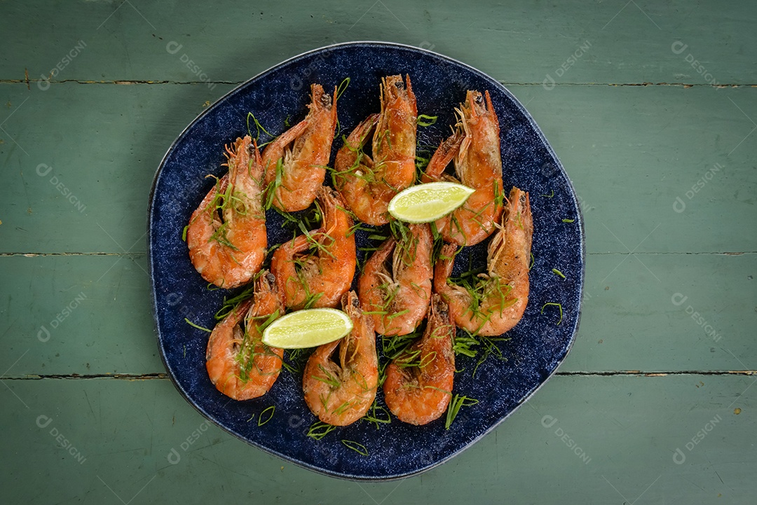 Camarão salteado com alho e azeite num prato azul escuro sobre uma mesa de madeira pintada de verde. Comida brasileira muito consumida no litoral.