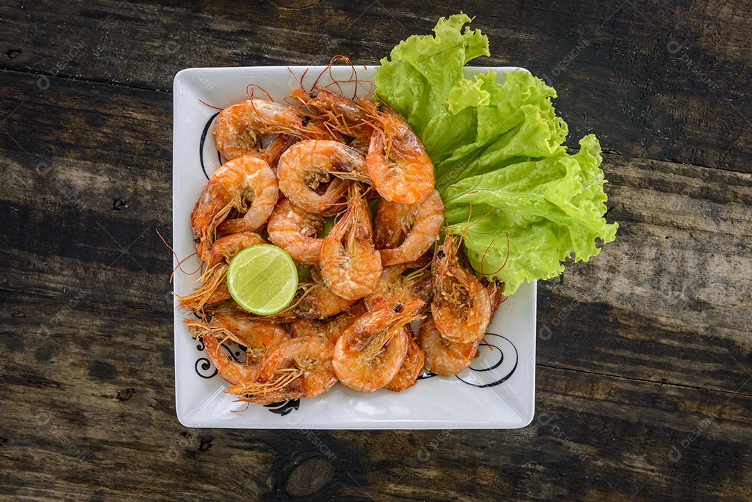 Camarão refogado com alho e azeite em prato branco sobre mesa de madeira. Comida brasileira muito consumida no litoral.