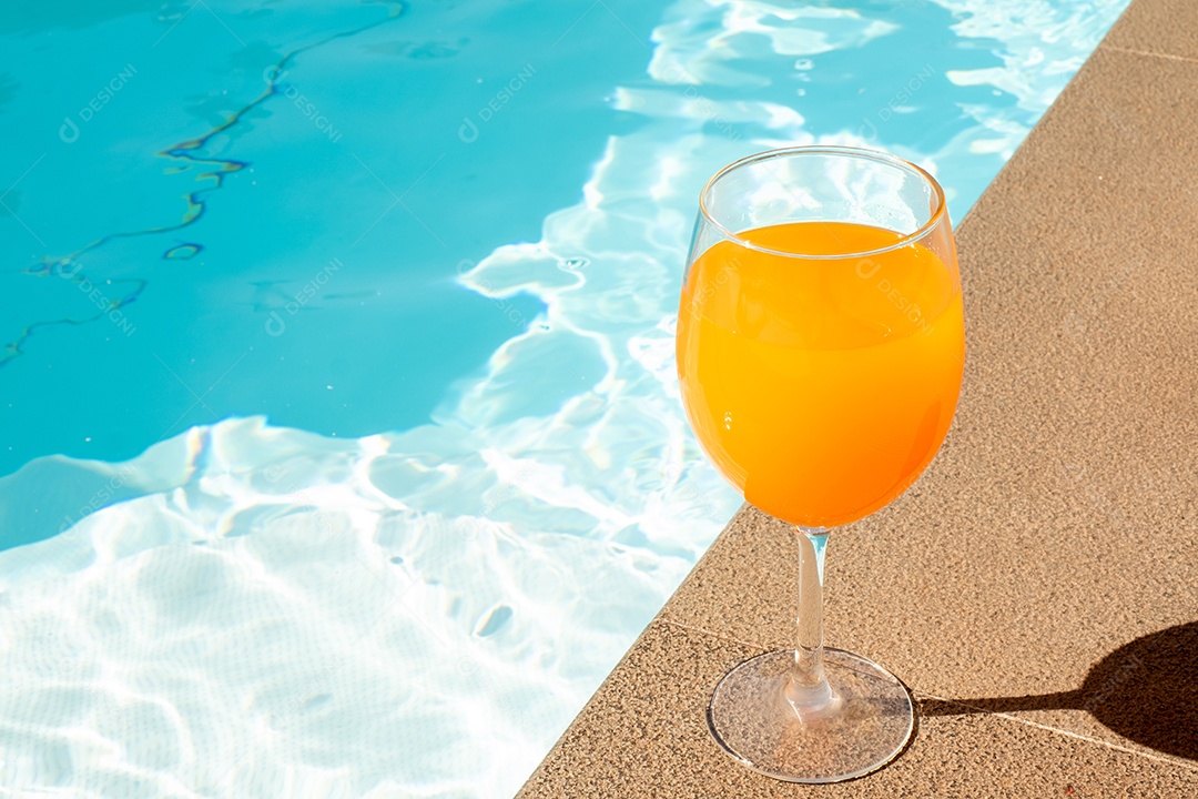 O suco de laranja na taça de vinho fica ao lado da piscina.